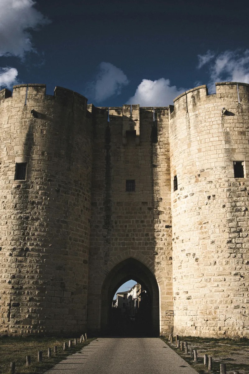 The medieval ramparts and the great cylindrical Tour de Constance of Aigues-Mortes rising above the flat Camargue, their pale stone glowing at golden hour with the salt lakes beyond. Aigues-Mortes, Occitanie, France.